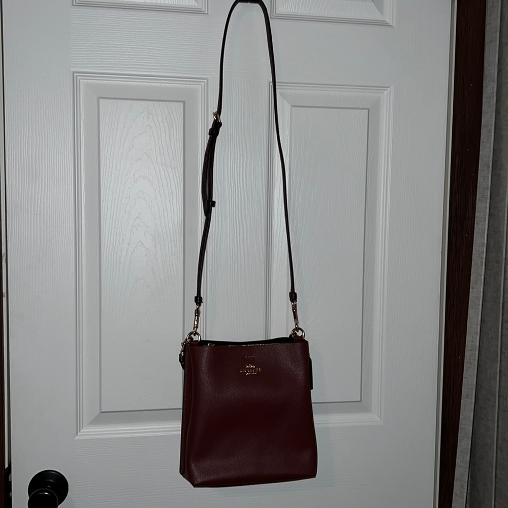 Burgundy convertible cross body Coach purse with snake print strap and handle.